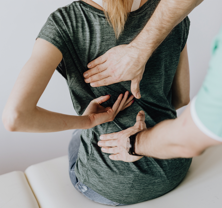 Person holding their back from the rear with a clinician pressing two hands onto the back