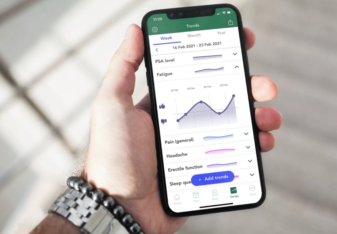 Person wearing a watch holding a mobile with an OWise screenshot showing how prostate cancer treatment side effects can be tracked in a graph format.
